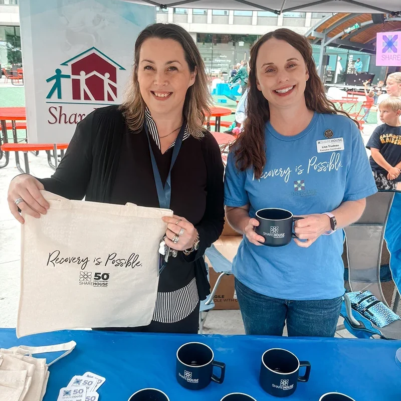 Sharehouse team at 50th anniversary booth holding Recovery is Possible merchandise