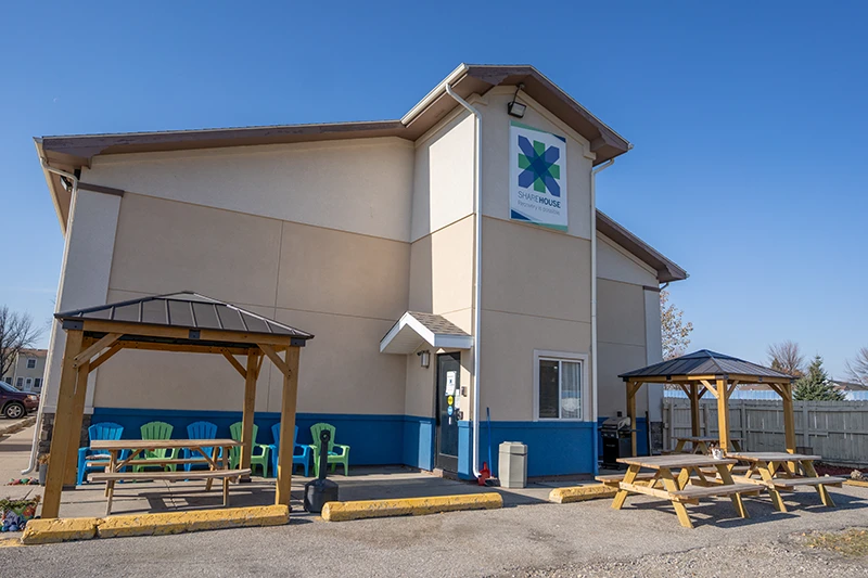 ShareHouse Grand Forks Residential Building with two wooden gazebos, one with a picnic table and the other with colorful chairs, set against a blue sky.