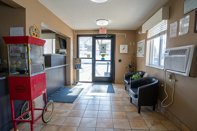 Interior lobby of ShareHouse Grand Forks building with a red popcorn machine, reception desk, two black armchairs, and a glass entrance door.