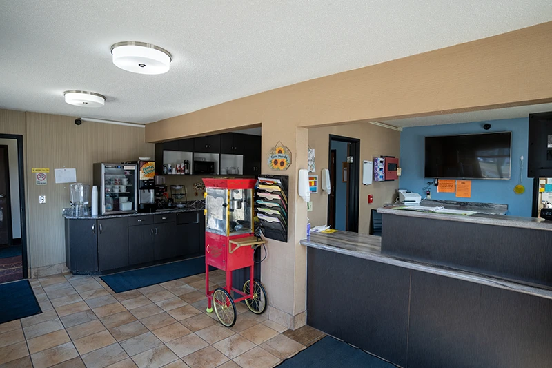 Interior view of ShareHouse Grand Forks Residential lobby featuring a reception desk, a snack and beverage area, a vintage popcorn machine, and large beige floor tiles.