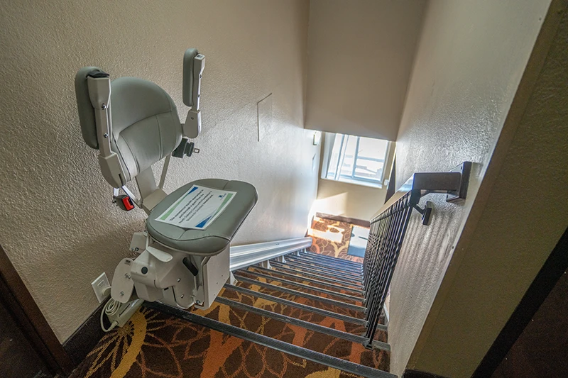 Interior stairwell featuring an accessible mobility lift and wall railing at ShareHouse Grand Forks Residential.