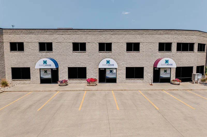 ShareHouse Fargo Outpatient Clinic Exterior with three entrances, colorful flower pots, and a parking lot, under a clear sky.