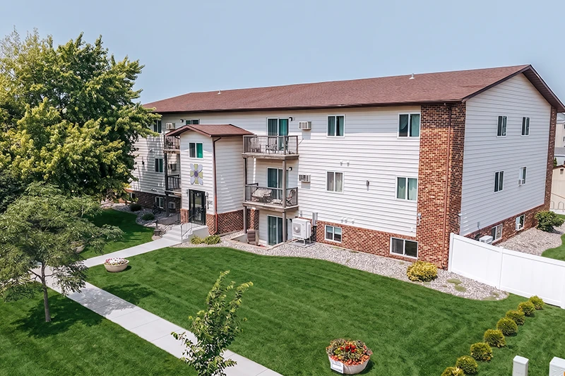 ShareHouse Recovery Residence Three-story building with white siding and red brick accents, surrounded by green lawn and decorative planters.