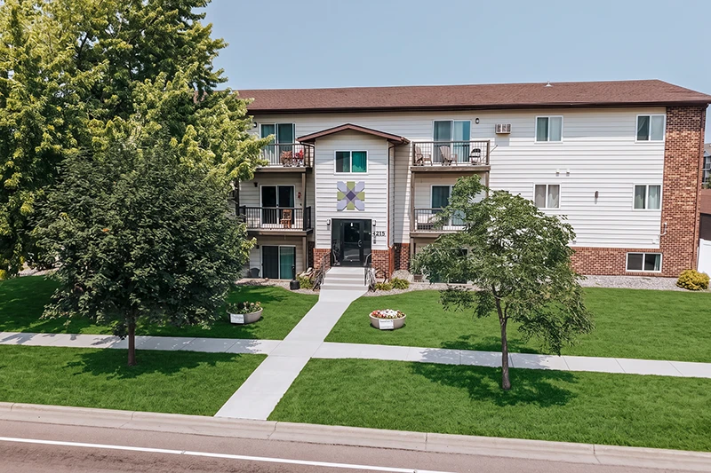 ShareHouse Recovery Residence Building with a central entrance, balconies, and decorative flower design on the facade, surrounded by green grass and trees.