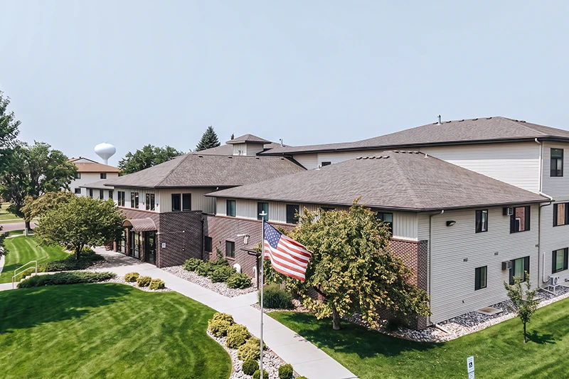 ShareHouse Fargo Residential Campus with brick and siding, surrounded by lush green grass and shrubs. An American flag is displayed in front, with a water tower visible in the background.